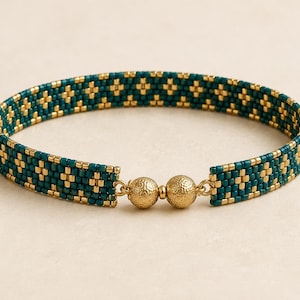 Peut inclure: Un bracelet en perles avec un motif géométrique répétitif composé de perles de rocaille bleu sarcelle et or métallique. Le bracelet est fermé par deux fermoirs magnétiques sphériques et texturés de couleur or qui se rejoignent au centre.