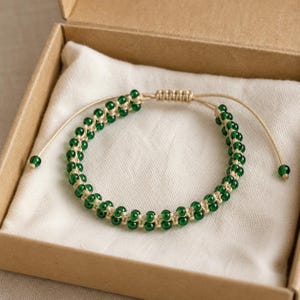 May include: A bracelet featuring two parallel rows of small, round, translucent emerald green beads woven onto a light beige cord. The design includes an adjustable sliding knot closure and two single green beads at the ends of the pull strings.