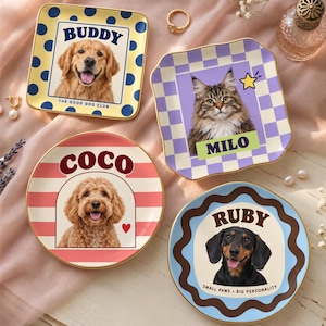 May include: Four ceramic trinket dishes featuring custom pet portraits. One square yellow dish with blue dots says BUDDY THE GOOD DOG CLUB. One square purple checkered dish says MILO. One round pink striped dish says COCO. One round wavy blue dish says RUBY SMALL PAWS BIG PERSONALITY.