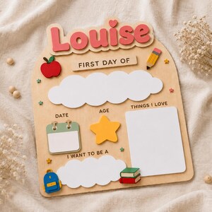 May include: A wooden arch-shaped sign with the name Louise in pink letters at the top. It features the text FIRST DAY OF, DATE, AGE, THINGS I LOVE, and I WANT TO BE A. Includes cutouts of an apple, pencil, calendar, star, backpack, and books.