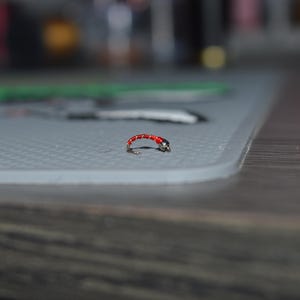 May include: A small red and silver fly fishing lure with a hook.