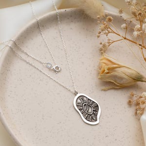 May include: A silver necklace featuring an irregular, organic-shaped pendant with a textured surface. The pendant displays a clock face design with Roman numerals and central hands. The piece includes a delicate silver chain with a spring ring clasp.