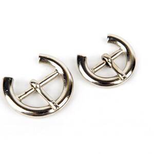 May include: Two silver metal belt buckle closures. The buckles are shaped like a half circle with a metal bar across the centre.