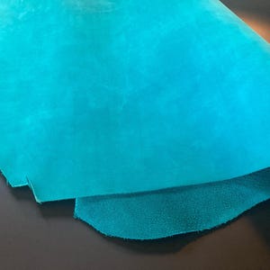 May include: A piece of teal blue leather with a smooth, slightly textured surface. The leather is folded in half, revealing the underside.