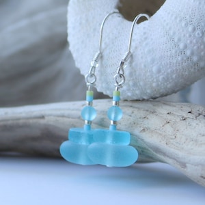 Peut inclure: Une paire de boucles d'oreilles pendantes avec des perles de verre de mer bleu empilées avec des accents argentés et de petites perles jaunes et bleues.