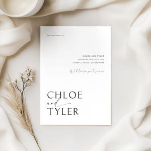 Close-up of a minimalist wedding invitation featuring clean typography with candlelit styling in the background