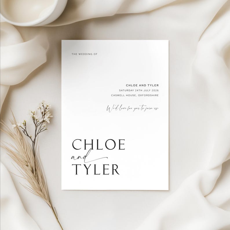 Close-up of a minimalist wedding invitation featuring clean typography with candlelit styling in the background