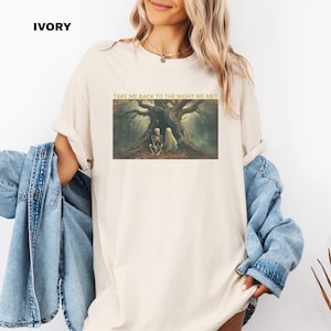 Puede incluir: Una camiseta de color crema con el texto "Take me back to the night we met" impreso en la parte delantera. El texto está en color dorado y está rodeado por un gráfico de un esqueleto y un fantasma sentados debajo de un árbol.