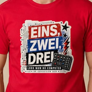 Puede incluir: Una camiseta roja con un diseño gráfico que presenta las palabras alemanas "Eins, Zwei, Drei" en blanco, azul y rojo. El diseño incluye una placa de circuito, una estrella y un rayo. También está presente el texto "LOOK MUM NO COMPUTER".