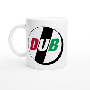 May include: White ceramic mug with a black and white circular design. The design features the word "DUB" in red, white, and green. The mug has a curved handle and is suitable for hot or cold beverages.