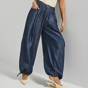 May include: A woman wearing a pale yellow halter top and dark blue denim pants. The pants have a high waist, large pockets, and gathered ankles. She is also wearing cream-colored slingback heels.