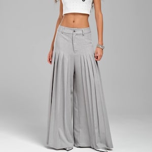 May include: A woman wearing a white cropped tank top with a small black heart design and gray pleated wide-leg pants.