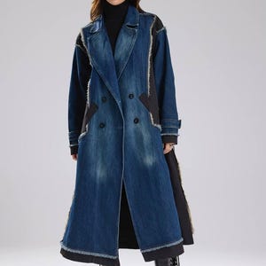 May include: A long, double-breasted denim coat with black accents and frayed edges. The coat features a classic lapel, button closures, and a long, flowing silhouette. The model is wearing a black turtleneck and boots.