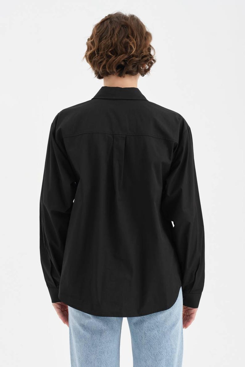 Puede incluir: Una camisa negra de manga larga con botones. La camisa tiene un cuello cl&aacute;sico, pu&ntilde;os abotonados y un dobladillo curvo. El modelo lleva vaqueros azul claro. La camisa est&aacute; hecha de una tela lisa y opaca.