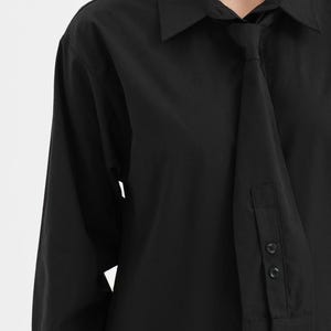 Puede incluir: Camisa negra de manga larga con un detalle de corbata &uacute;nico. La camisa presenta un cuello cl&aacute;sico y pu&ntilde;os abotonados. La corbata est&aacute; integrada en el dise&ntilde;o, creando un look moderno y elegante. La camisa est&aacute; hecha de una tela negra lisa y suave.