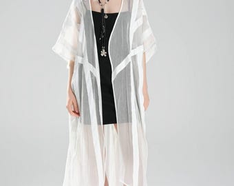 May include: A white, sheer, longline kimono-style jacket with vertical and horizontal stripe details. The jacket is worn over a black dress and paired with a black necklace and black sandals. The overall style is minimalist and modern.
