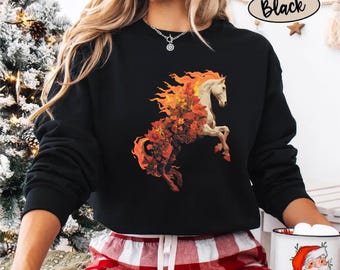 May include: A black long-sleeve sweatshirt featuring a graphic of a white horse with a mane and tail made of orange and red flames and autumn flowers. The sweatshirt has a crew neckline and is worn with red and white plaid pajama pants.