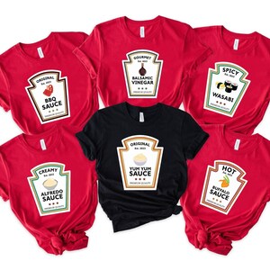 May include: A collection of five red t-shirts and one black t-shirt, each featuring a graphic design shaped like a condiment bottle label. The labels display various text including Original BBQ Sauce, Gourmet Balsamic Vinegar, Spicy Wasabi, Creamy Alfredo Sauce, Original Yum Yum Sauce, and Hot Buffalo Sauce.