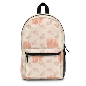 May include: A cream-colored backpack with a black handle and zipper. The backpack features a repeating pattern of pink leaf designs and brushstrokes. A black mesh pocket is on the side.