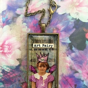 May include: A glass pendant necklace with a bronze chain. The pendant features a vintage image of a young girl wearing a crown and wings. The text "Art Fairy" is visible on the pendant.