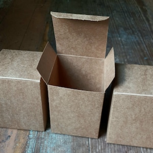 May include: Three brown cardboard boxes, one is open and the other two are closed. The boxes are on a wooden surface.
