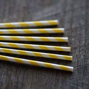 May include: A close-up of six yellow and white striped paper straws on a wooden surface.