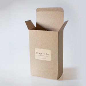May include: A brown cardboard box with the lid open. The box has a white label with the text "Wraps & Co." and the words "Delicately Woven Wraps & More".