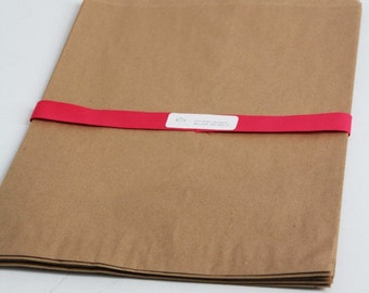 May include: A stack of brown paper bags tied together with a bright pink ribbon. The ribbon has a white label with the text "GIFT WRAP & GREETING CARDS" printed on it.