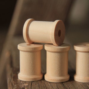 May include: Four wooden spools stacked on a wooden surface. The top spool is lying horizontally, while the three spools below are standing upright.