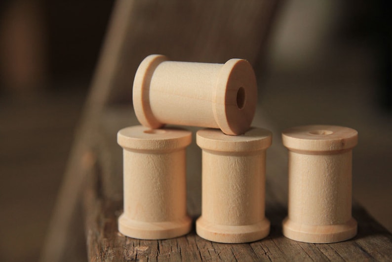 May include: Four wooden spools stacked on a wooden surface. The top spool is lying horizontally, while the three spools below are standing upright.