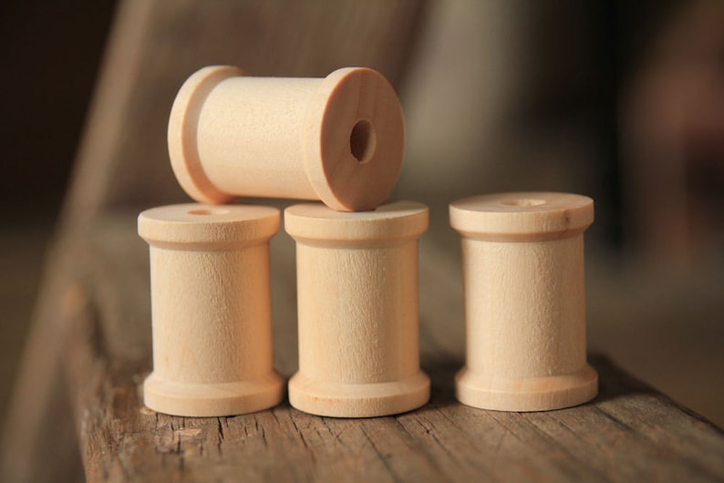 May include: Four wooden spools, stacked on a wooden surface. The top spool is lying horizontally, while the three spools below are standing upright.