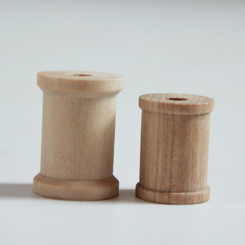 May include: Two wooden spools, one larger than the other, both with a smooth, light brown finish. The spools are made of wood and have a hole in the center.