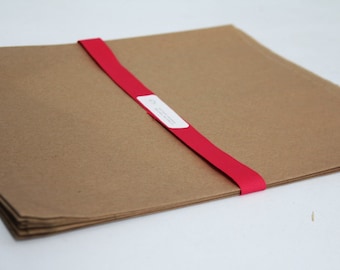 May include: A stack of brown paper sheets tied together with a red ribbon. The ribbon has a white label with text.