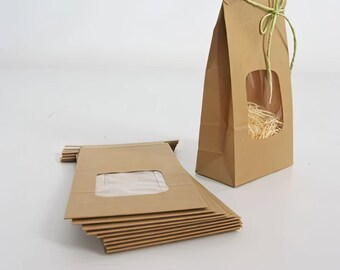 May include: A stack of brown paper bags with a clear window, and a single brown paper bag with a clear window and a green ribbon tied around the top.