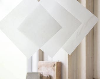 May include: Three white sheets of paper hanging on a clothesline with wooden clothespins. The sheets are hanging in front of a window with books on the windowsill.