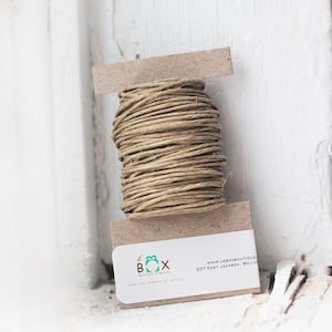 May include: A spool of natural twine wrapped around a cardboard tube. The twine is a light brown color and is perfect for wrapping gifts or crafts. The cardboard tube has a label that says "be BOX boutique" and "love the moment of giving". The label also includes the website address "www.leboxboutique.com" and the address "207 East Jackson, Bolivar".