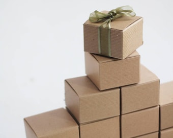 Puede incluir: Una pila de cajas de regalo de cartón marrón con una cinta verde en la caja superior.