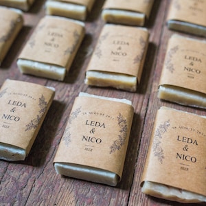 An assortment of mini hotel sized soap favors with kraft wraps around the soaps.  The wrap design has a floral edging and they list the bride and groom's name, wedding date and the soap scent.
