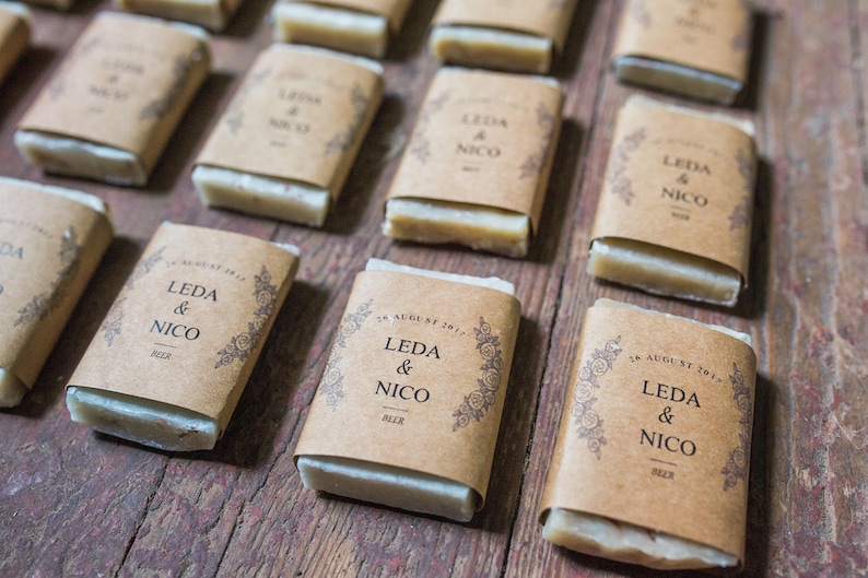 An assortment of mini hotel sized soap favors with kraft wraps around the soaps.  The wrap design has a floral edging and they list the bride and groom's name, wedding date and the soap scent.