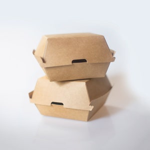 May include: Two brown cardboard takeout containers stacked on top of each other. The containers are designed for holding food, such as sandwiches or burgers.