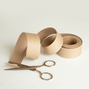 brown kraft paper ribbon roll, unwinding, laying next to scissors on a white background