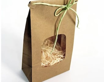 May include: A brown paper gift bag with a rectangular window revealing shredded paper filler. The bag is tied with a green twine bow. The bag is made of brown paper.