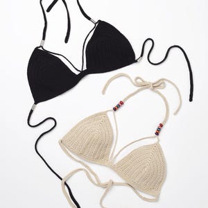 May include: Two crocheted bikini tops, one black and one beige. The beige top has colorful beads on the straps.