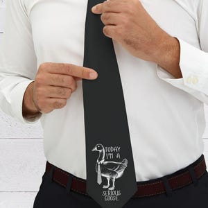 Puede incluir: Una corbata negra con un gráfico de ganso blanco y el texto "Today I'm a Serious Goose".