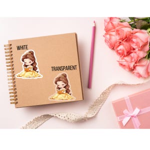 Puede incluir: Dos pegatinas con una princesa de dibujos animados leyendo un libro, una blanca y otra transparente, se muestran en un cuaderno de espiral. Los textos "WHITE" y "TRANSPARENT" est&aacute;n encima de las pegatinas. Un l&aacute;piz rosa, rosas rosas y una caja de regalo rosa con una cinta blanca tambi&eacute;n est&aacute;n en la imagen.