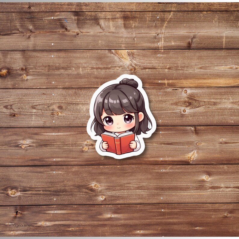 Puede incluir: Una pegatina con una ilustraci&oacute;n de estilo anime de una ni&ntilde;a con cabello oscuro en un mo&ntilde;o, leyendo un libro rojo. La pegatina tiene un borde blanco y est&aacute; sobre un fondo de madera.