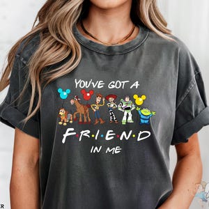 A woman wearing a gray t-shirt with a graphic design featuring characters from the TV show "Friends" and the text "You've Got a Friend in Me".
