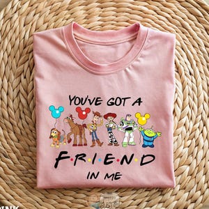 A pink t-shirt with a graphic design featuring characters from the animated series "Toy Story" and the text "You've Got a Friend in Me".