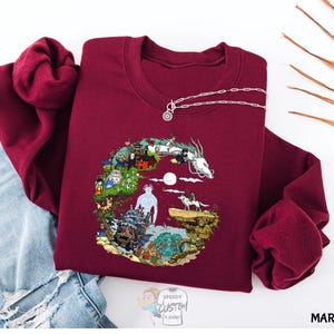 A maroon sweater with a colorful, illustrated design depicting various elements such as a castle, animals, and a moon.