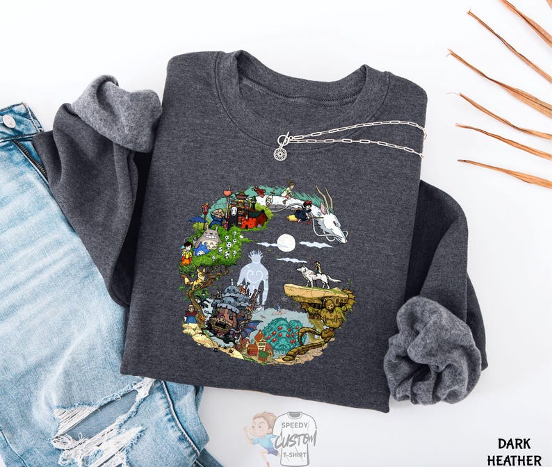 A gray sweatshirt with a colorful, illustrated design depicting various elements such as a castle, a dragon, and a unicorn, along with a necklace and a pair of jeans.